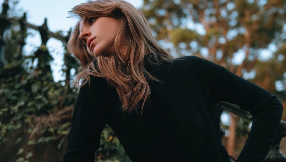 Woman in black long-sleeve top looking over shoulder outdoors during golden hour.