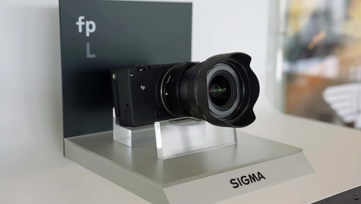 Sigma lens mounted on fp L camera body displayed on white pedestal with branding.