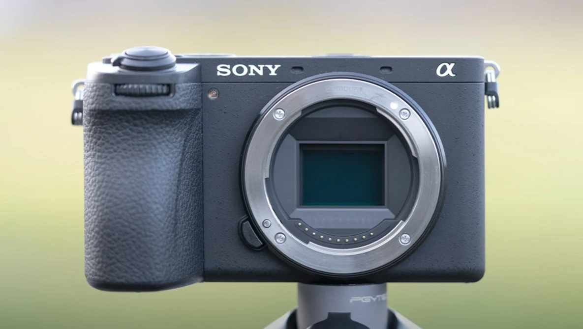 Sony Alpha mirrorless camera body with open lens mount displayed against a blurred yellow-green background.