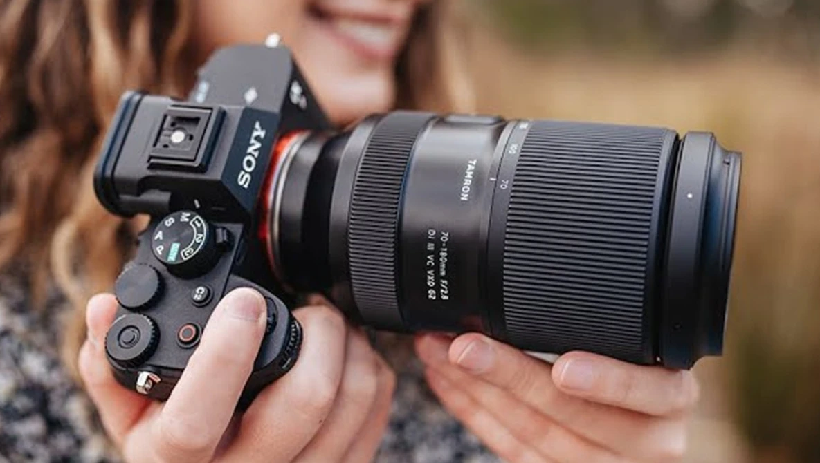 Photographer holding a Sony mirrorless camera with a telephoto lens and external flash mounted on top.
