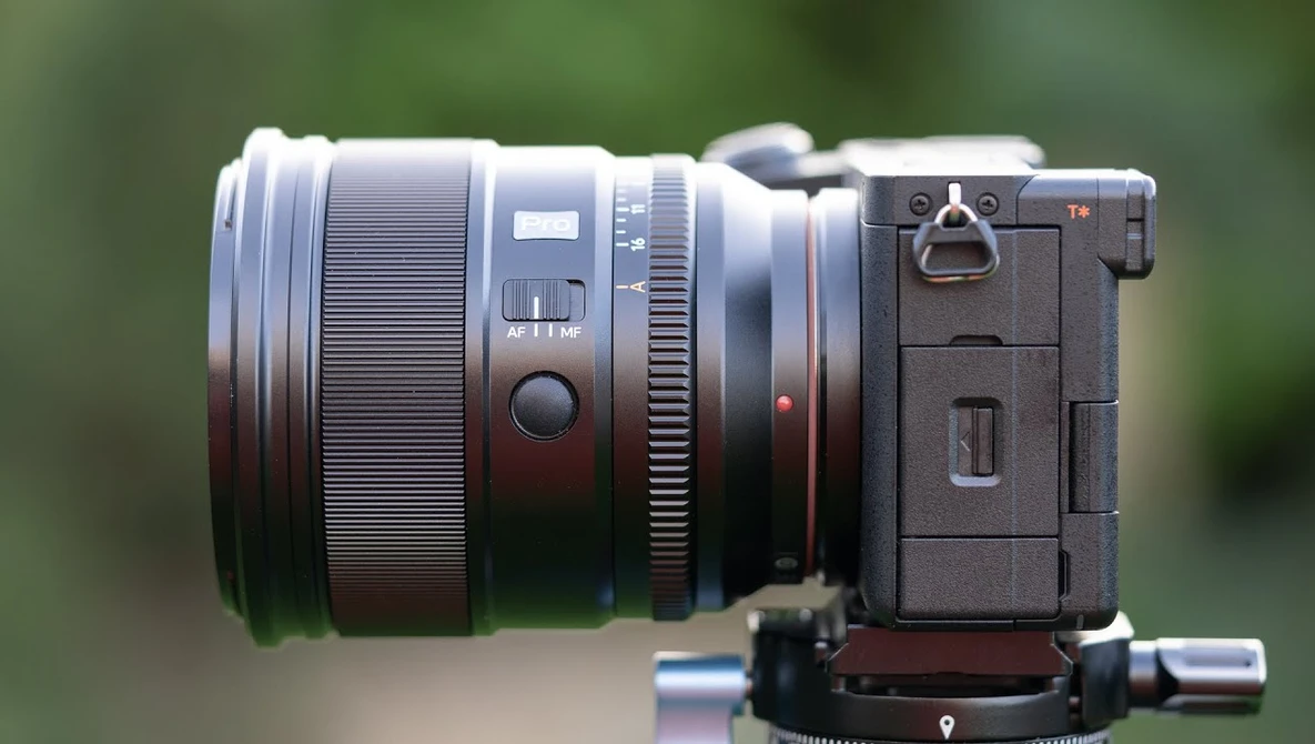 Mirrorless camera with large telephoto lens mounted on gimbal head, photographed against blurred green background.