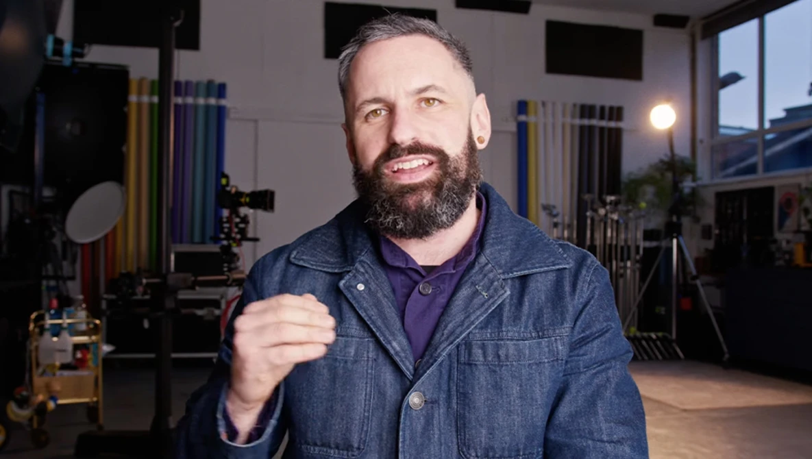 Bearded man in denim jacket smiling at camera in professional studio setting.