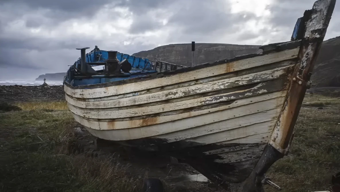 Weathered wooden fishing boat beached on barren grassland with mountains in background.