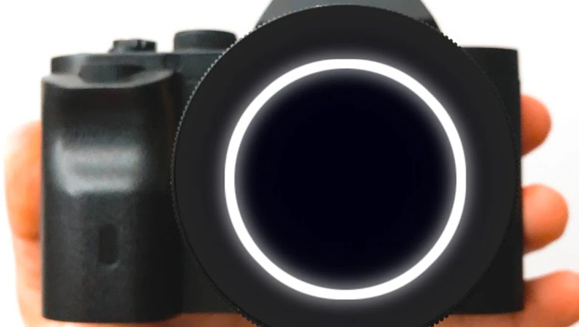 Compact camera with black body and orange grip held in hand, featuring illuminated circular lens ring.