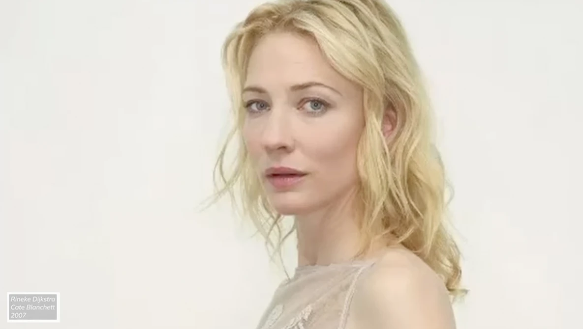 Blonde woman with wavy hair in neutral studio portrait against white background.