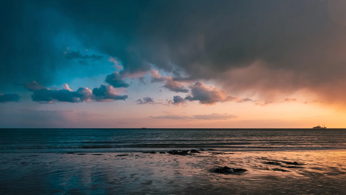 Dramatic sunset over a calm ocean with golden and blue-tinted clouds reflecting on the water.