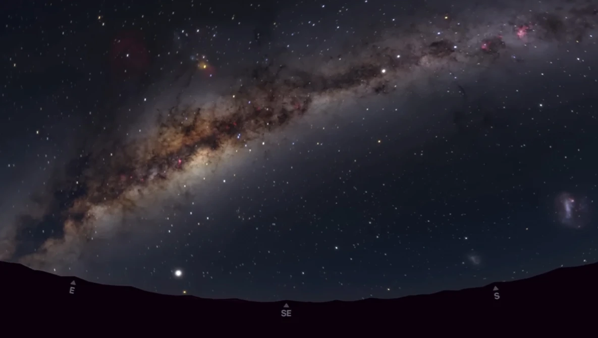 The Milky Way galaxy stretches diagonally across a starry night sky above a dark silhouetted landscape.