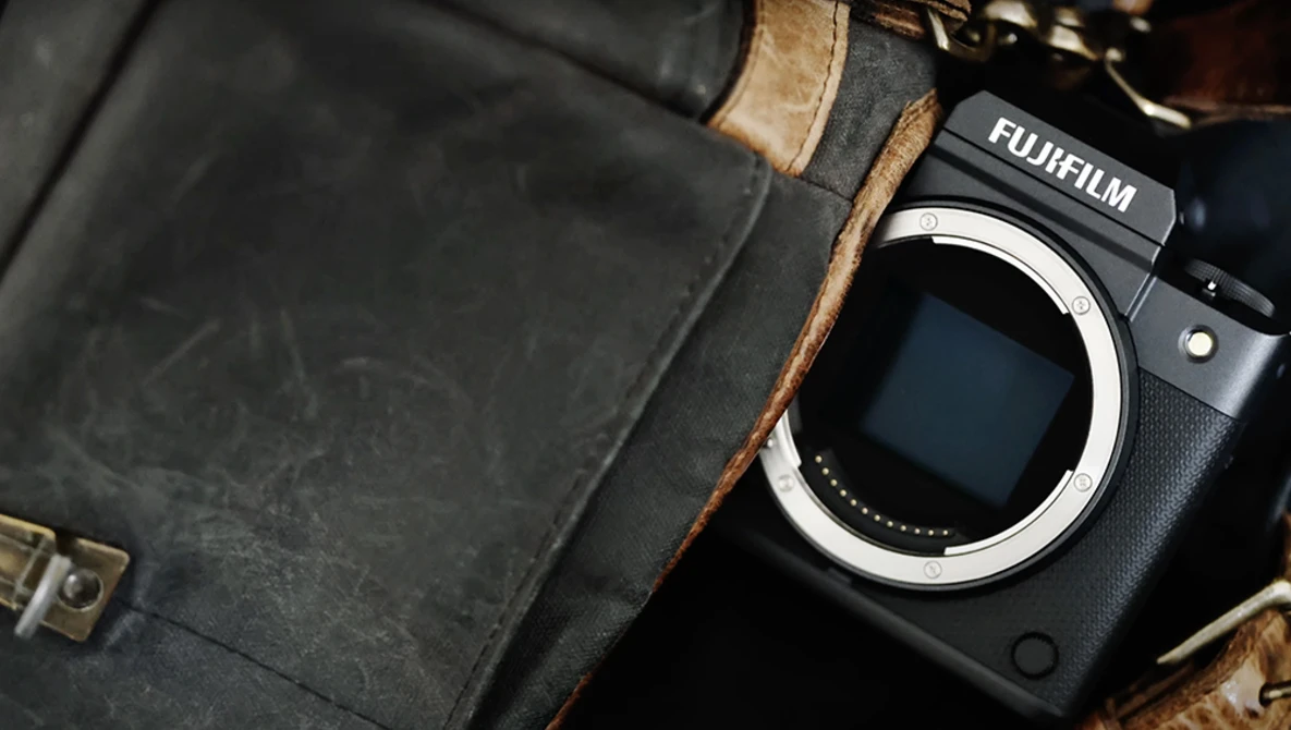 Fujifilm mirrorless camera body next to vintage leather camera bag with brass hardware.
