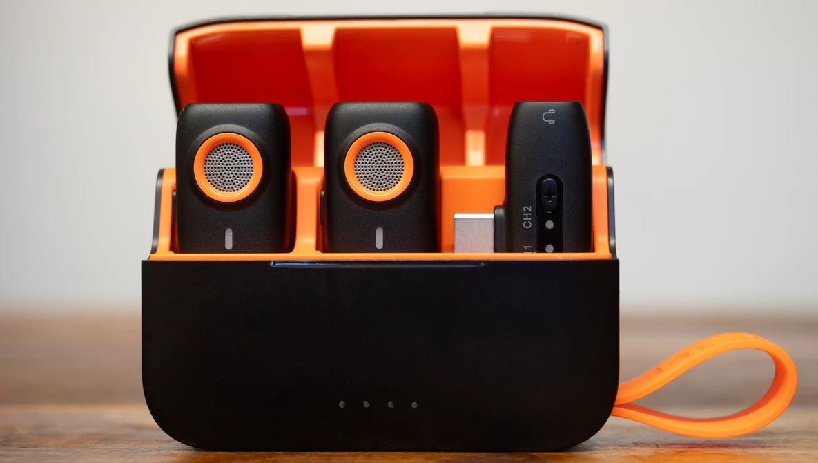 Portable wireless microphone system with charging case displaying two black microphones with orange accents and a receiver unit.