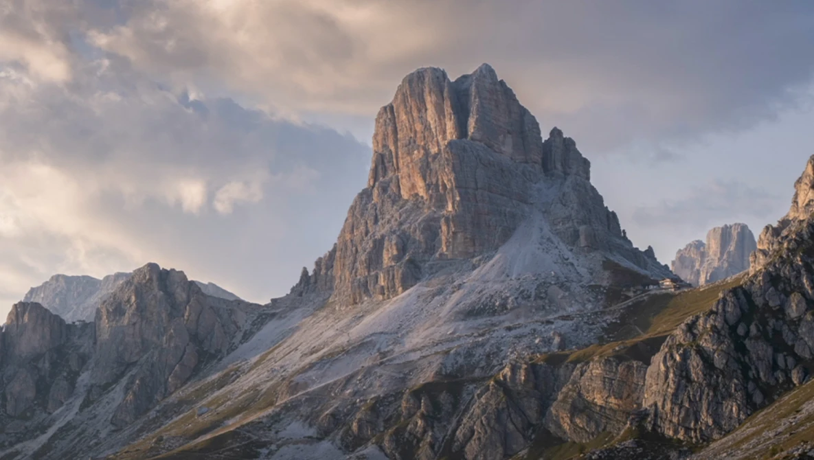 Dramatic alpine peak with steep columnar rock formations and early snow in golden hour light.