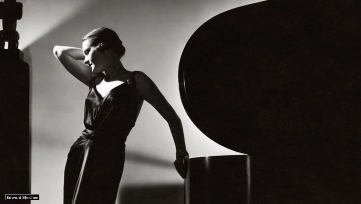 Woman in dark dress poses against geometric black shapes in high-contrast studio lighting.