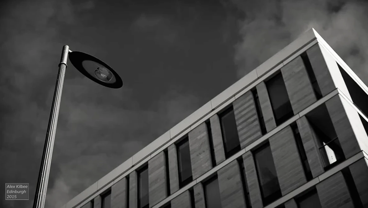 Street lamp against dramatic cloudy sky with modernist building facade featuring vertical window lines.