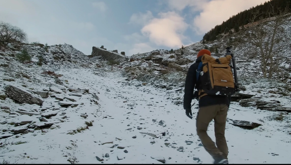Backpacker hiking across snowy alpine terrain with yellow and brown pack on their back.