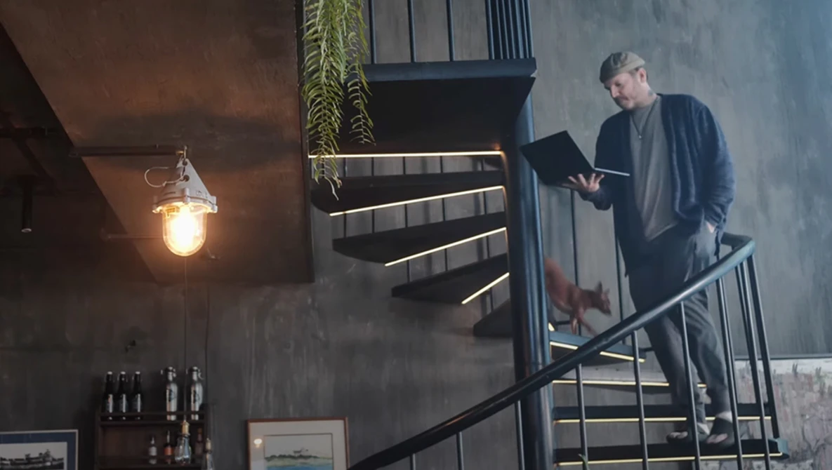 Man on industrial metal staircase reading a document while warm pendant light glows nearby.