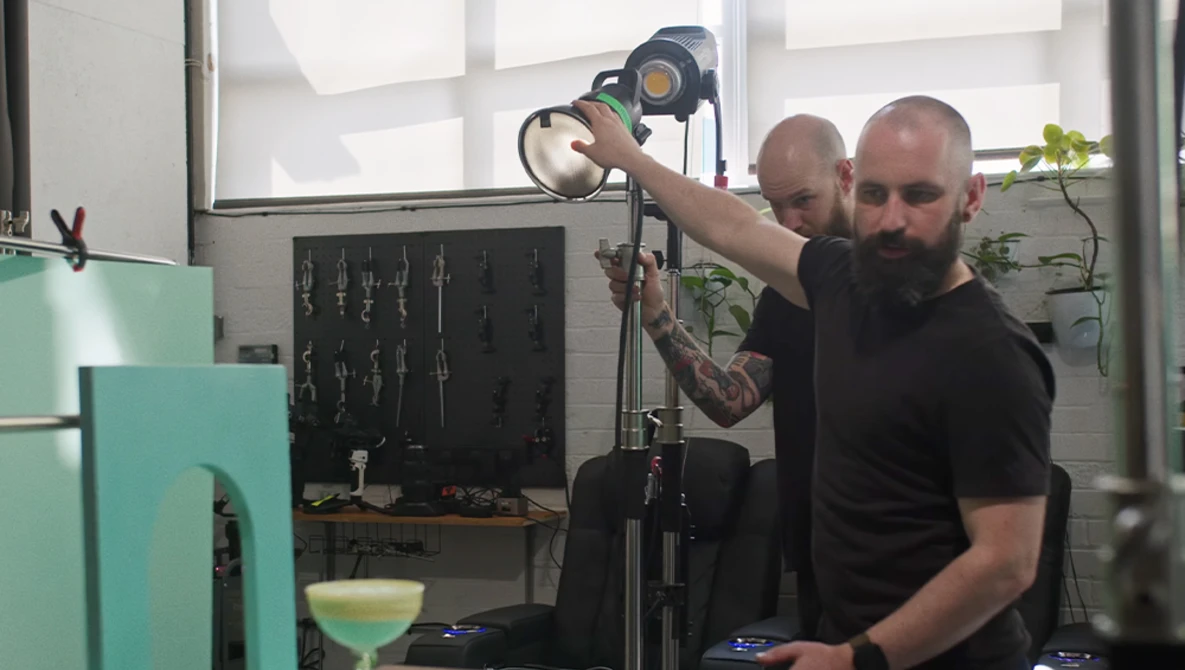 Two photographers adjusting a studio light on a stand during a production setup.