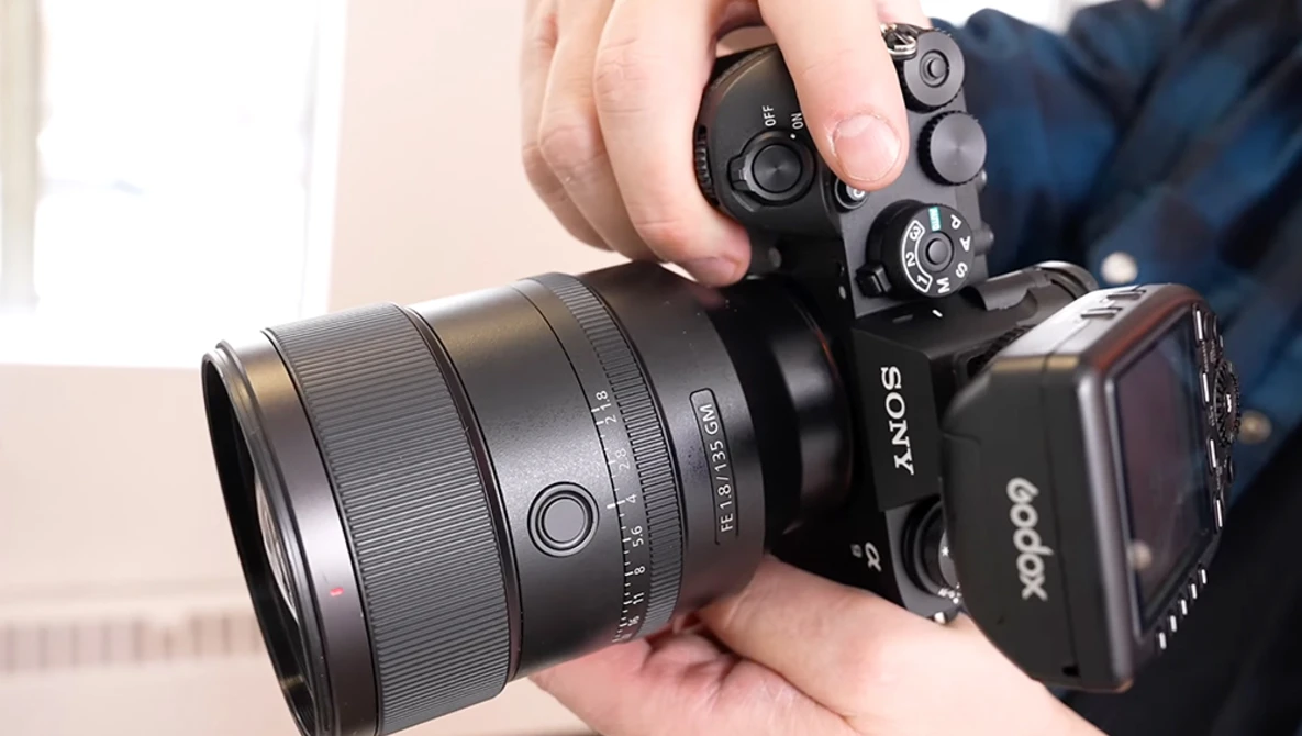 Hands holding a Sony mirrorless camera with attached lens and external flash unit.