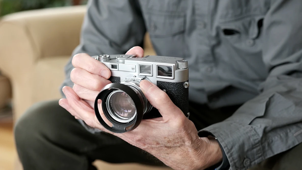 Hands holding a vintage rangefinder camera with a wide-angle lens attached.