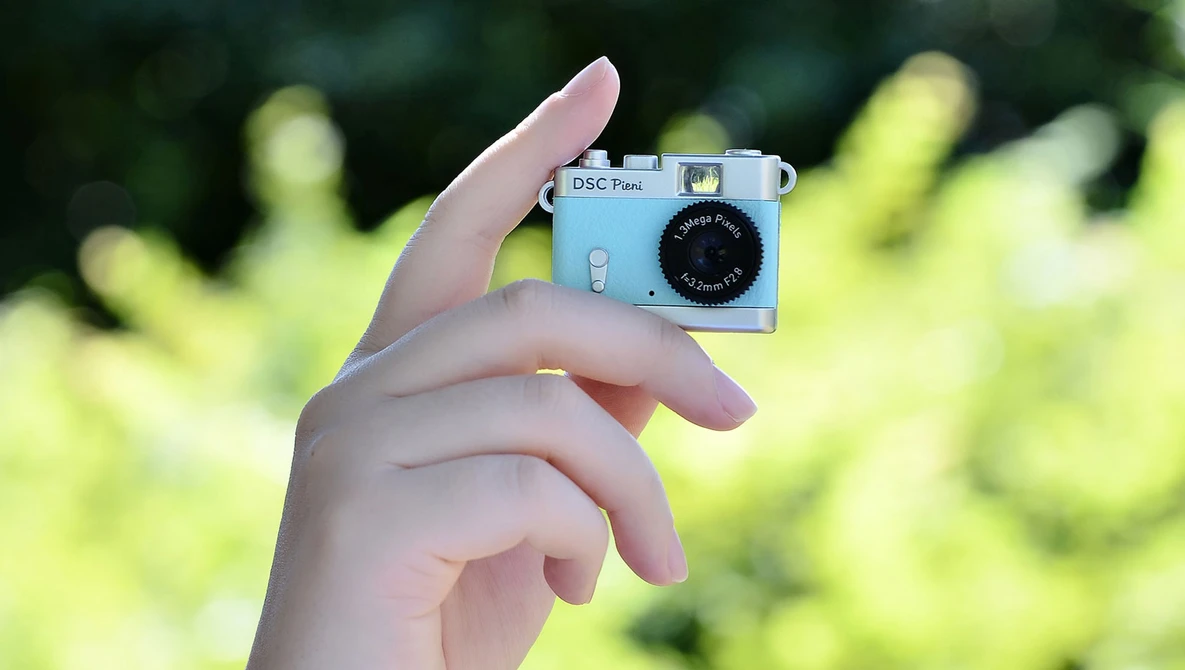 Hand holding a light blue vintage compact camera against a blurred green foliage background.