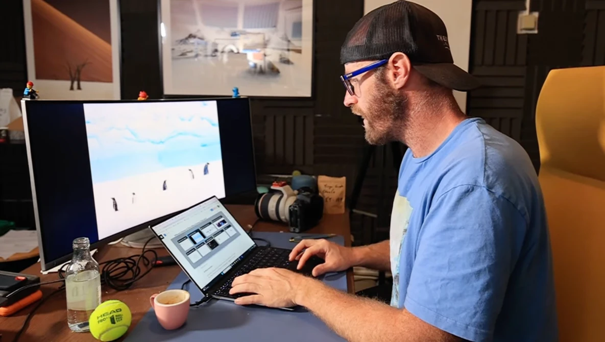 Photographer working at desk with monitor displaying landscape image and tablet for editing.