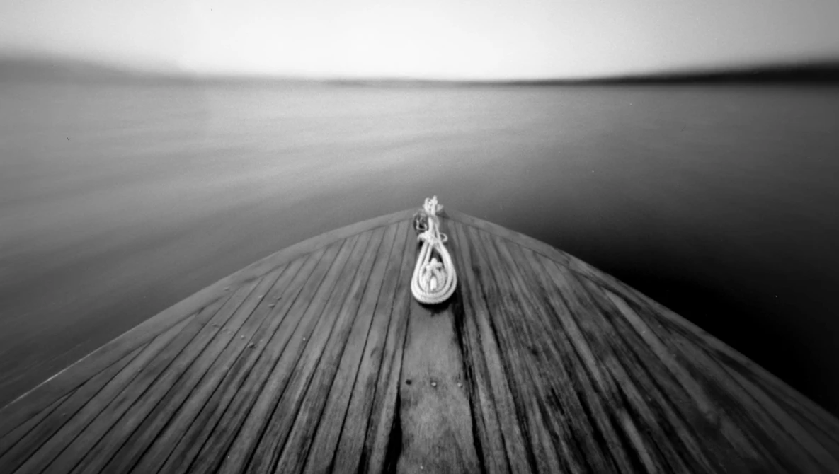 A single pulley attached to the center line of a wooden dock stretches toward calm water in black and white.