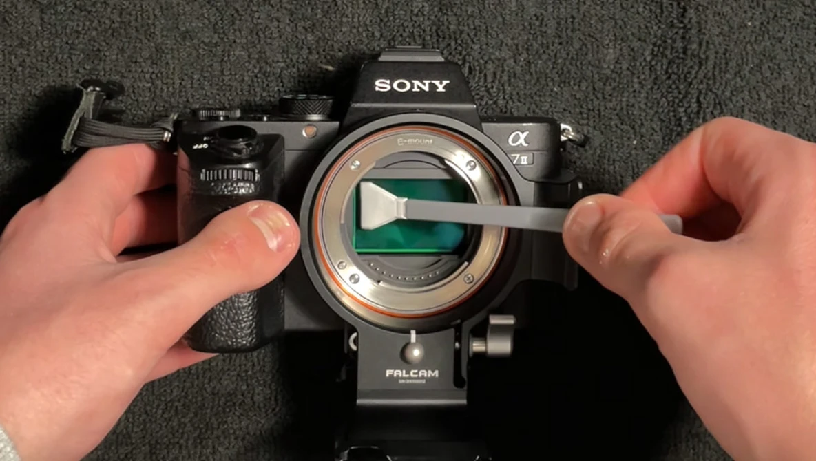 Hands demonstrating sensor cleaning on a Sony Alpha camera with visible mirror and sensor elements.