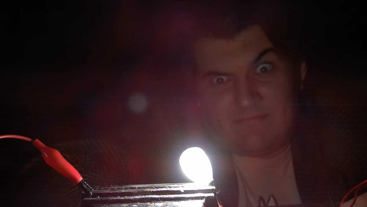 Person holding a bright LED light source close to camera in dark environment with red ambient lighting.