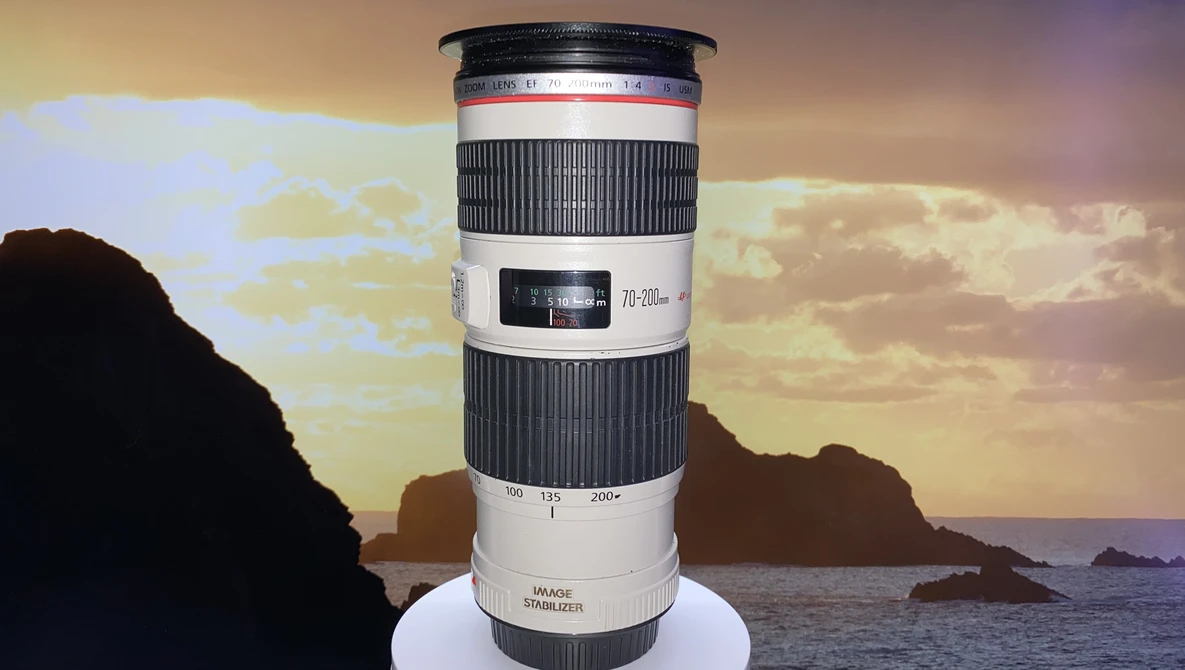 Canon EF 70-200mm f/2.8L telephoto lens displayed against a coastal sunset with rocky islands.