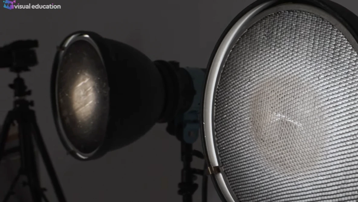 Two studio light fixtures with reflectors positioned against a dark gray background, one with visible dome reflector and one with honeycomb grid.