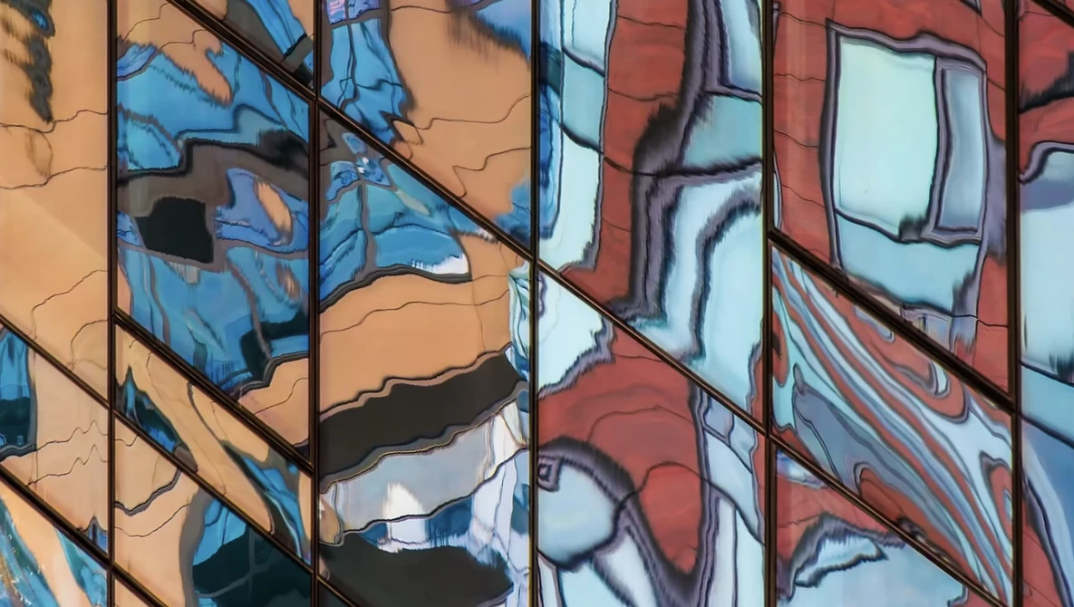 Reflections of blue sky and building facades in glass windows of a modern building.