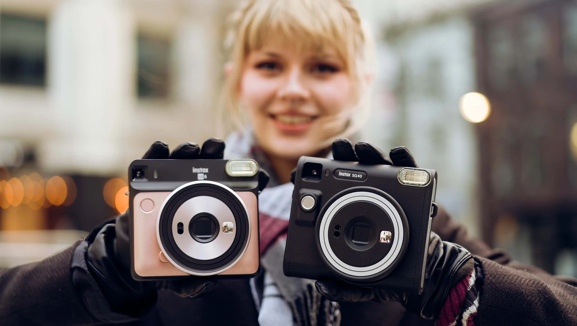 Child holding two vintage instant film cameras with black and beige bodies in an urban outdoor setting.