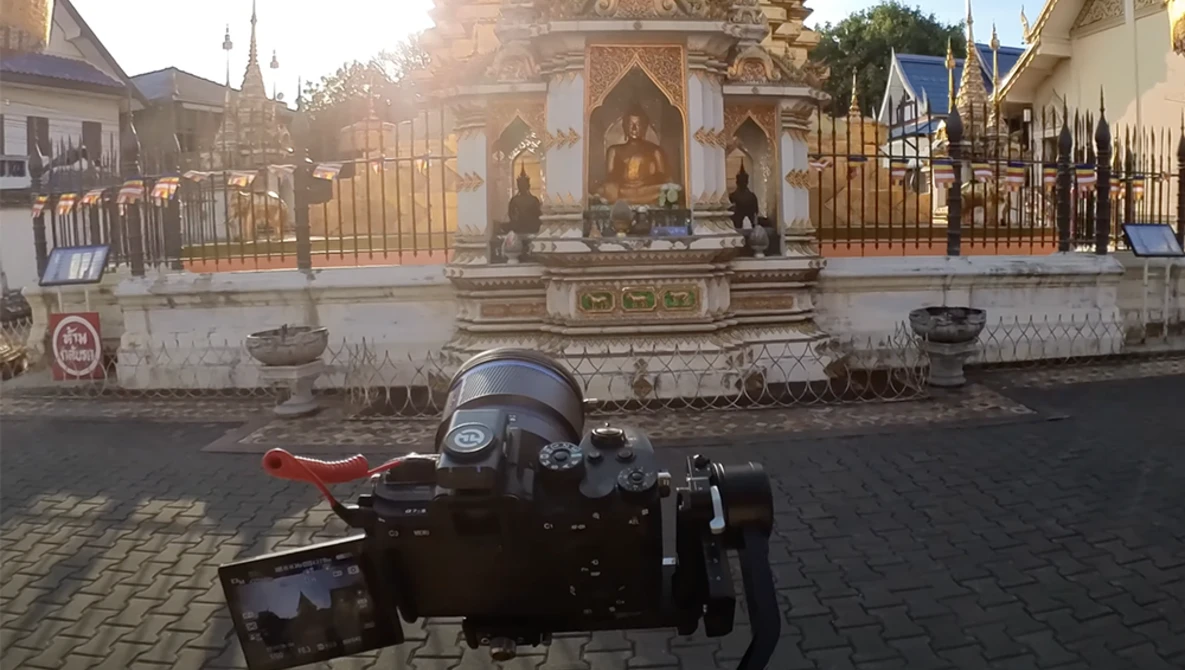 Camera on tripod with articulating monitor facing an ornate Buddhist temple with golden spires and white walls.