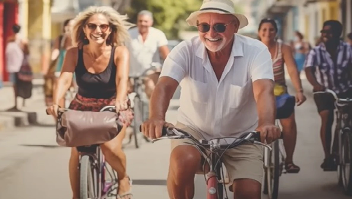 Couple riding bicycles down a sunny street lined with pedestrians and colorful buildings.