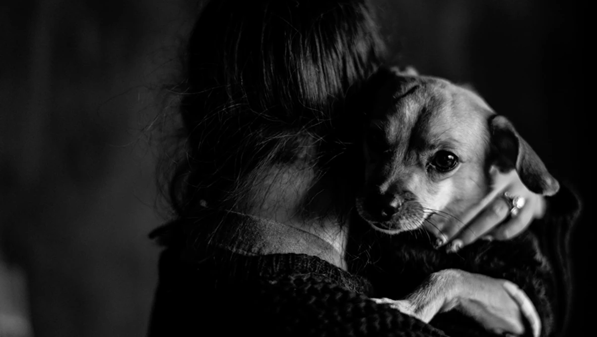 Person holding a small dog over their shoulder in a high-contrast black and white portrait.