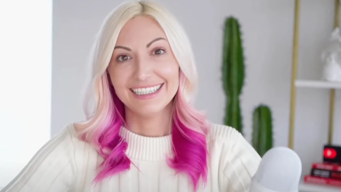 Portrait of a woman with platinum blonde and magenta ombre hair smiling at camera in studio setting.