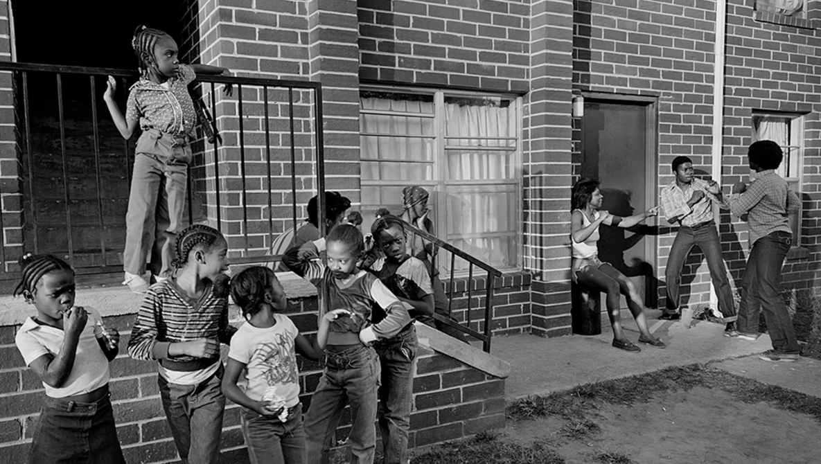 Children playing in an urban alley beside a brick building in this black and white street photograph.