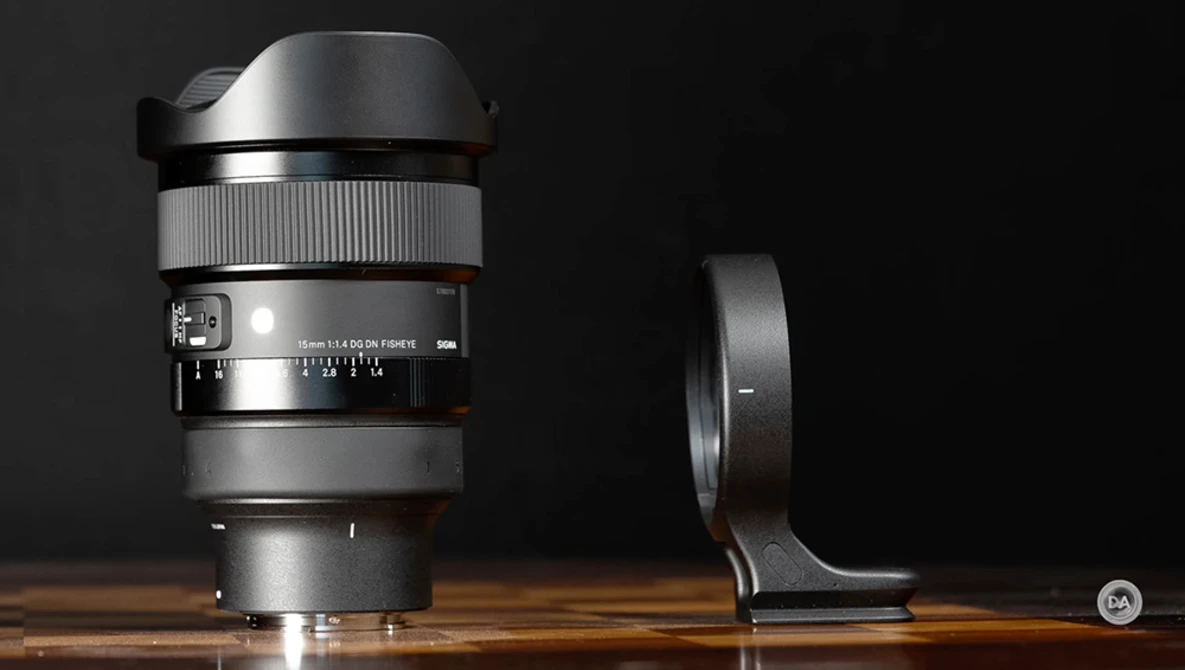 Wide-angle lens with lens hood and tripod collar mounted on wooden surface against black background.