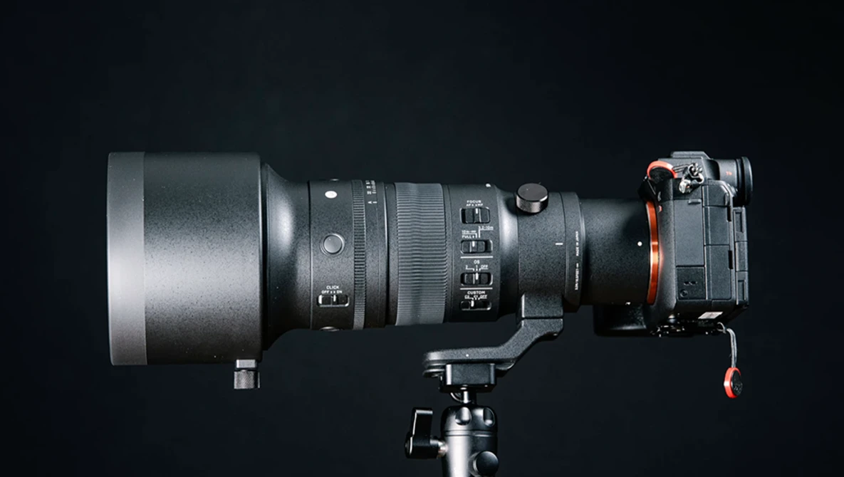 Professional camera lens mounted on tripod head with focus and zoom rings visible against dark background.