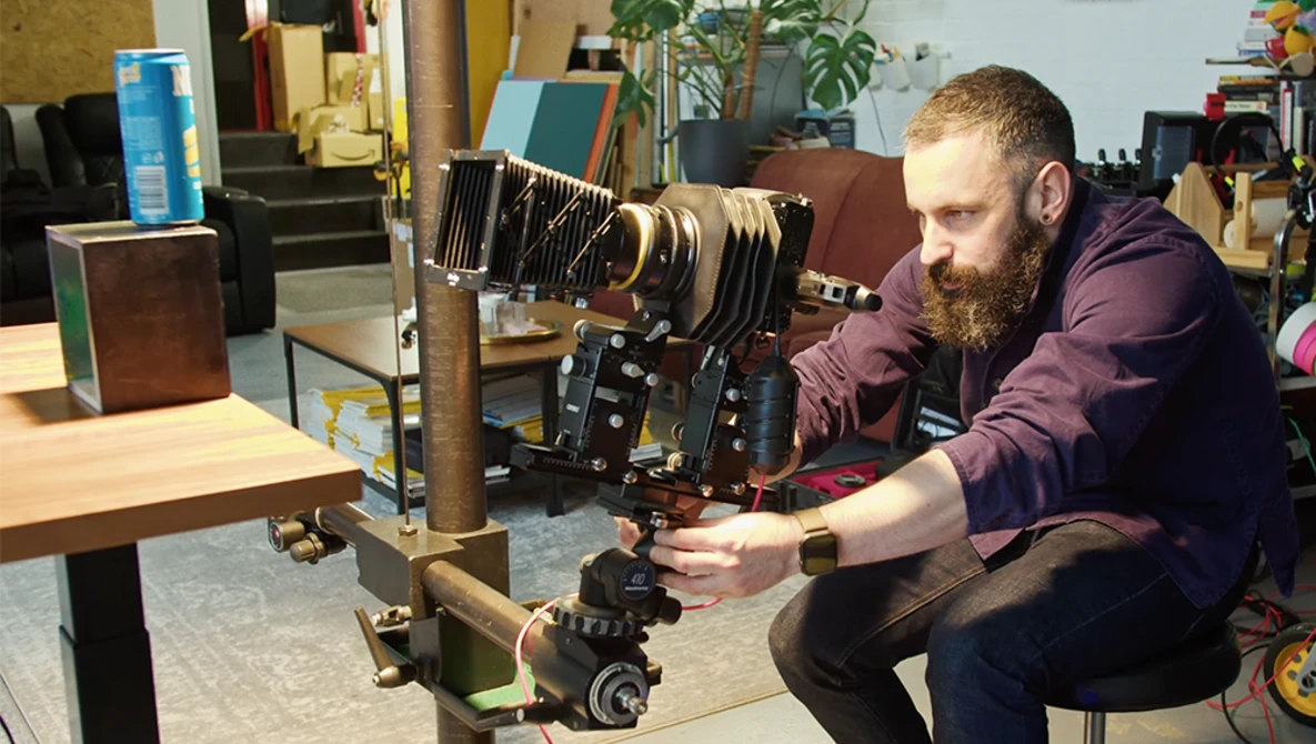 Photographer adjusting a large format camera mounted on a wooden stand in a studio workspace.