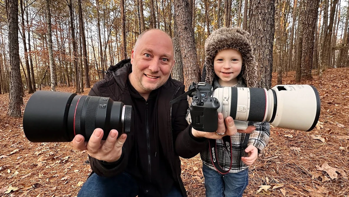 Adult and child holding professional camera lenses outdoors in a forest setting.
