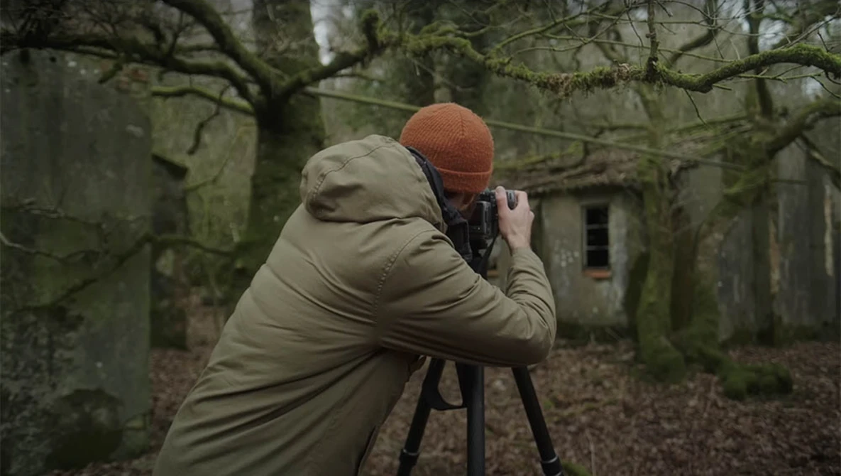 Photographer with camera on tripod shooting in overgrown forest ruins.