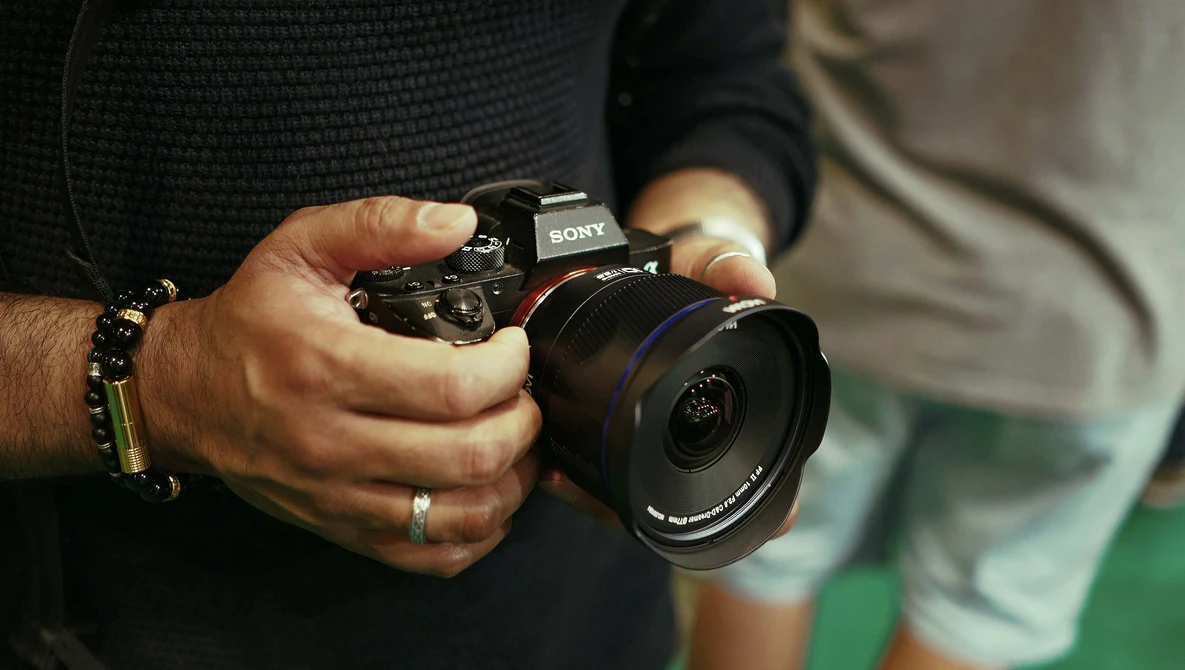 Photographer's hands holding a Sony mirrorless camera with wide-angle lens attached.