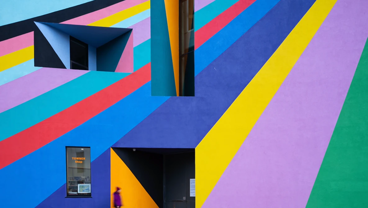 Colorful geometric mural with diagonal stripes in blue, pink, yellow, purple, and green, featuring black architectural elements and doorways.