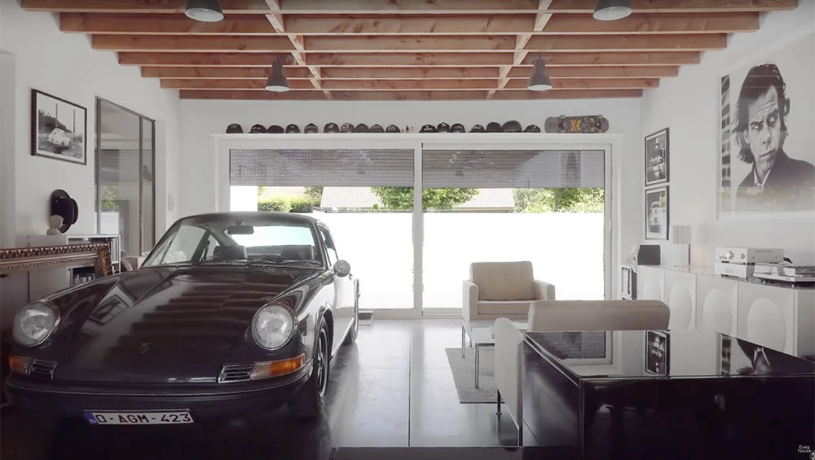 Black Porsche 911 displayed in a minimalist white garage with exposed wooden ceiling beams.