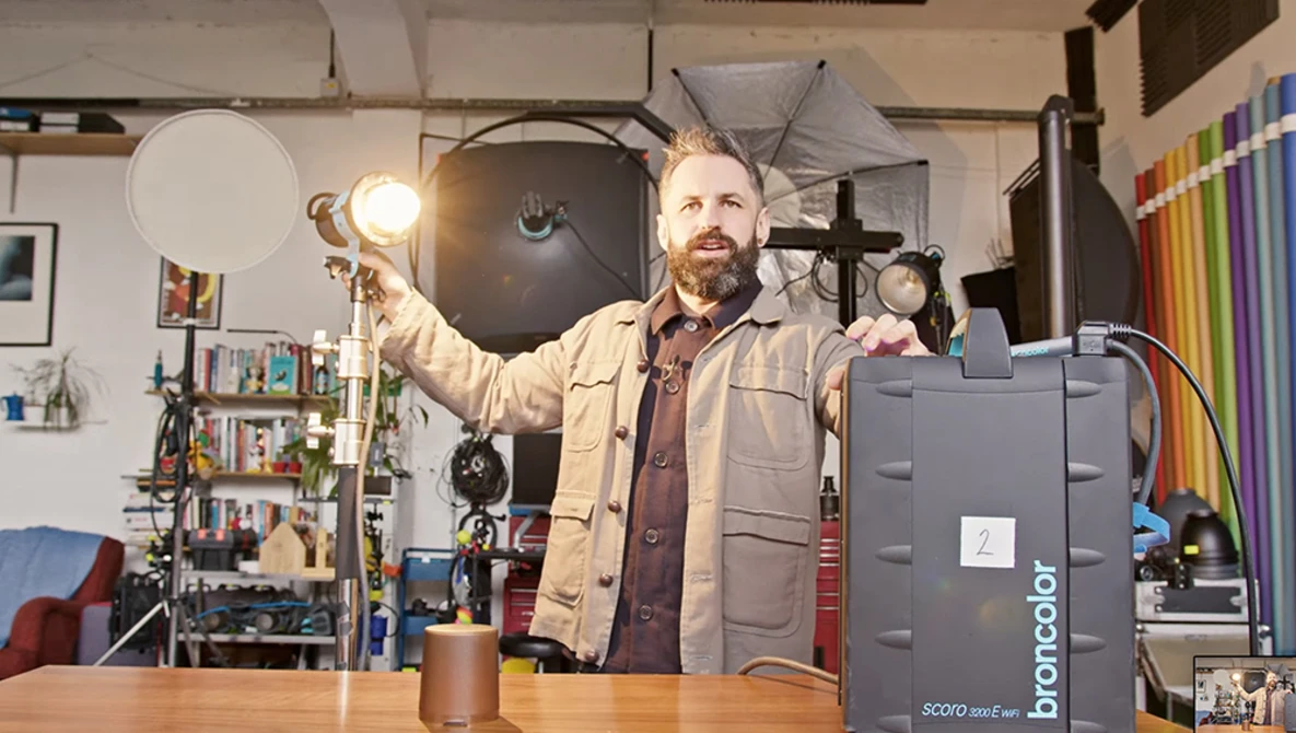 Photographer holding a reflector in a studio filled with lighting equipment and props.