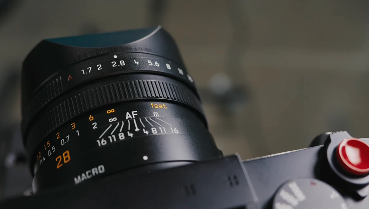 Close-up of a vintage manual focus lens showing aperture ring, focus scale, and macro marking.