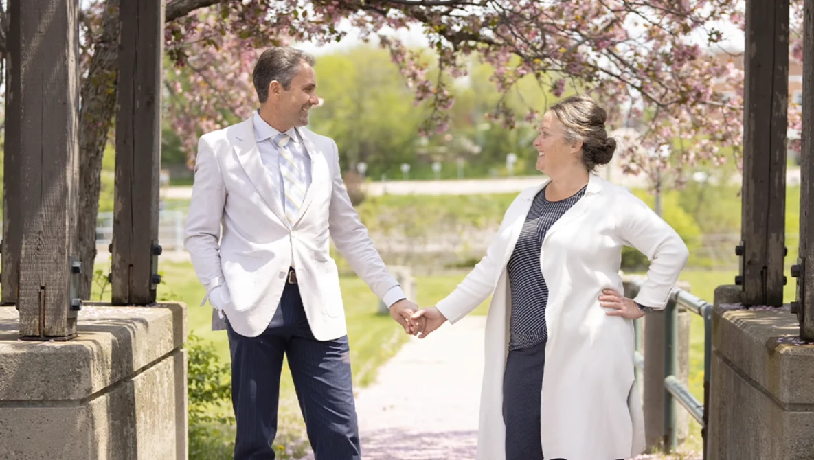 Couple holding hands under a wooden arbor with blooming cherry blossoms overhead.