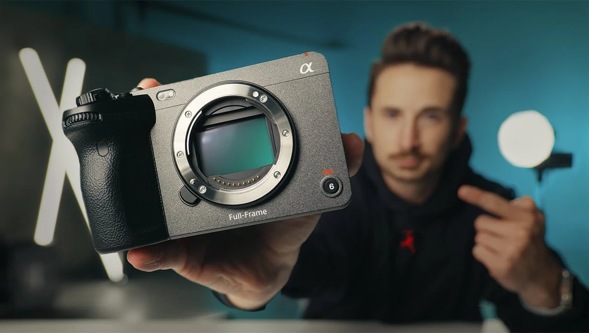 Photographer holding a mirrorless camera body with visible sensor and a ring light in studio setting.