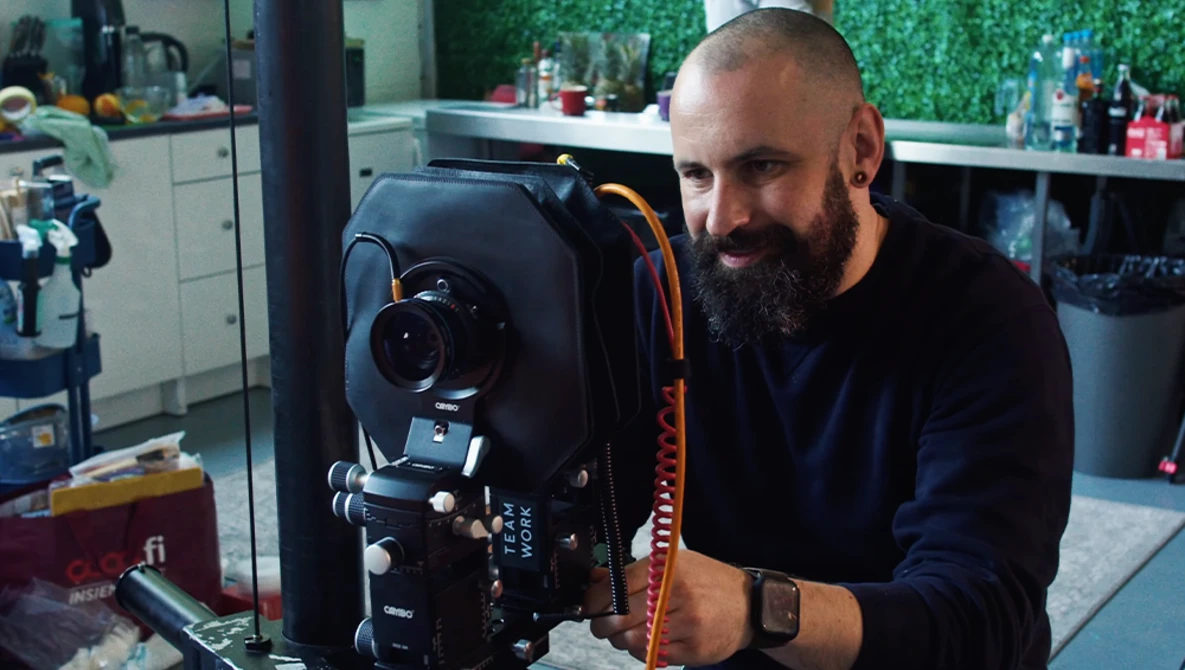 Photographer posing with professional cinema camera mounted on tripod in studio setting.
