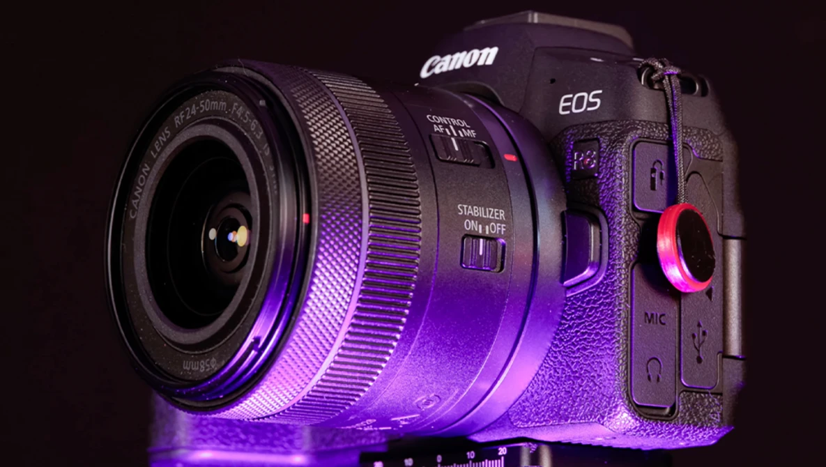 Canon EOS R5 mirrorless camera with attached lens, illuminated by purple and pink neon lighting against a dark background.