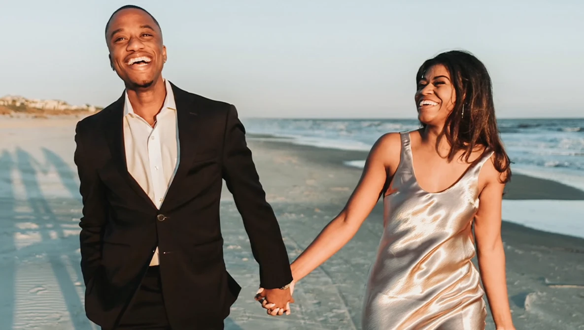 Couple holding hands while walking on a beach at sunset.
